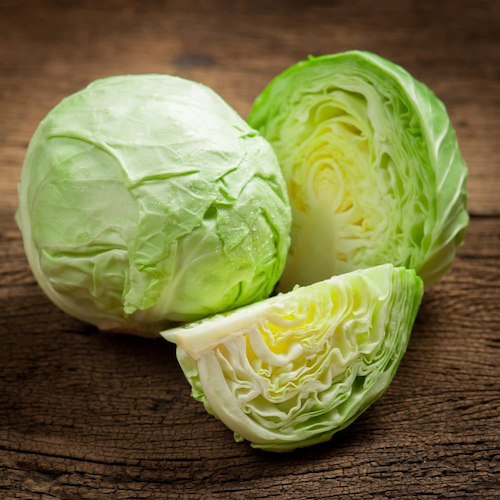 Fresh green cabbaged cut in half and wedges on a wooden table.