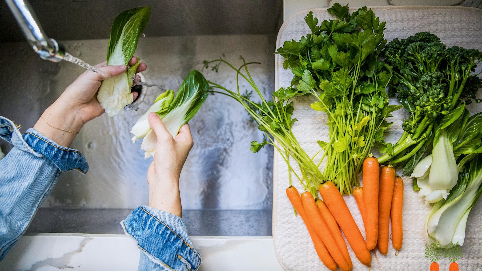 Close-up of summer vegetables being cleaned by hand under a steady stream of water.