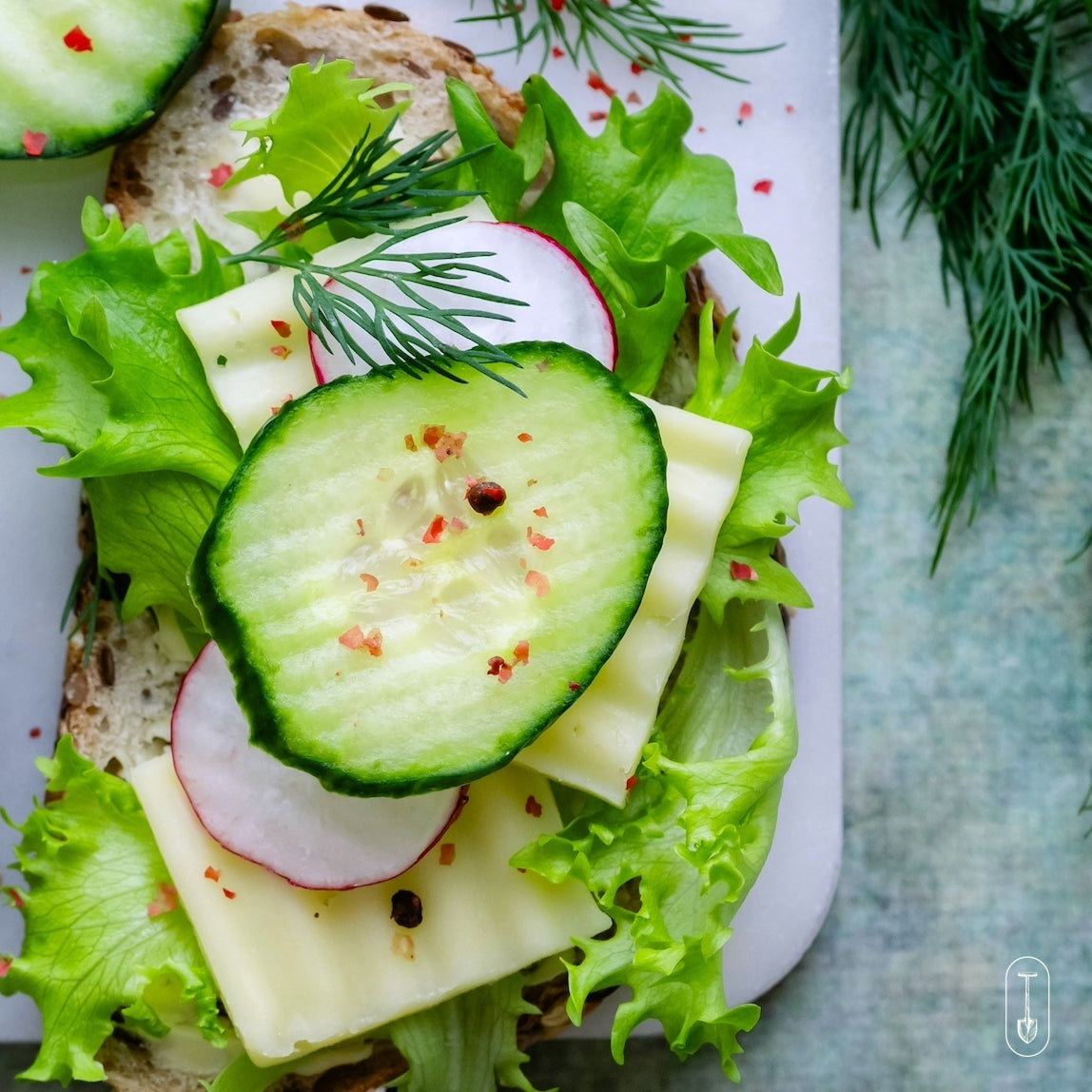 ibrant sandwich topped with sliced cucumber, radish, and fresh lettuce in a detailed close-up.